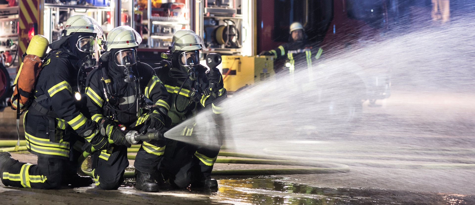 3 Feuerwehrmänner halten einen Löschschlauch, aus dem Wasser spritzt